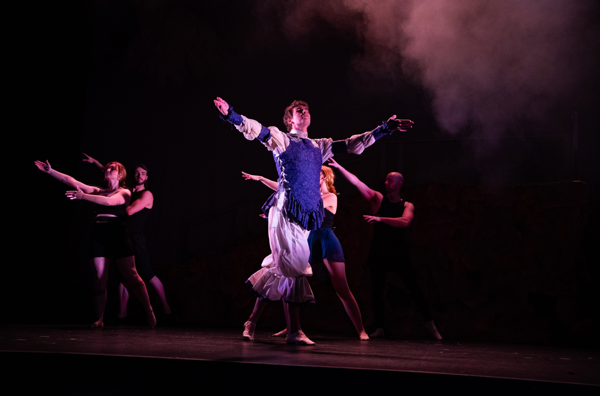 A group of people are dancing on a stage in a dark room.