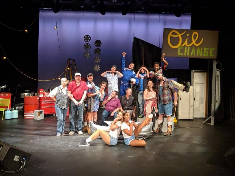 A group of people are posing on a stage in front of an oil change sign