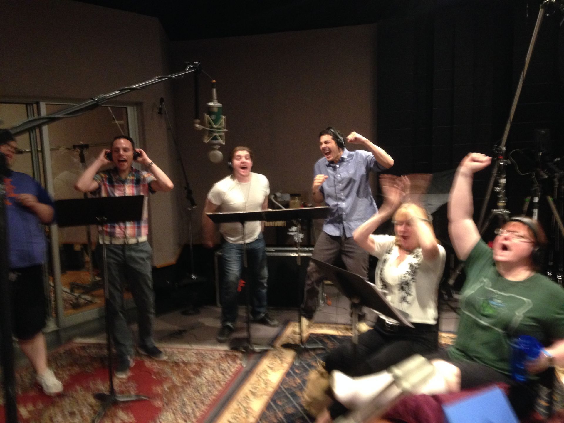 A group of people are singing into microphones in a recording studio