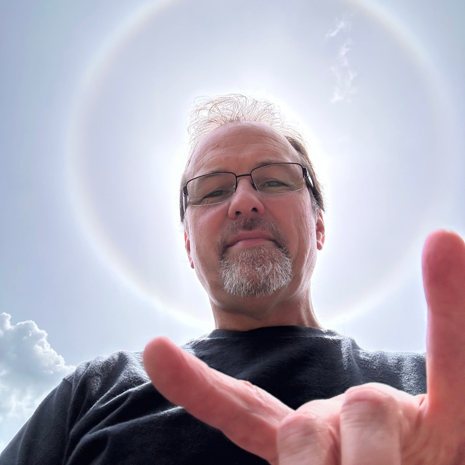A man with glasses and a beard is making a peace sign