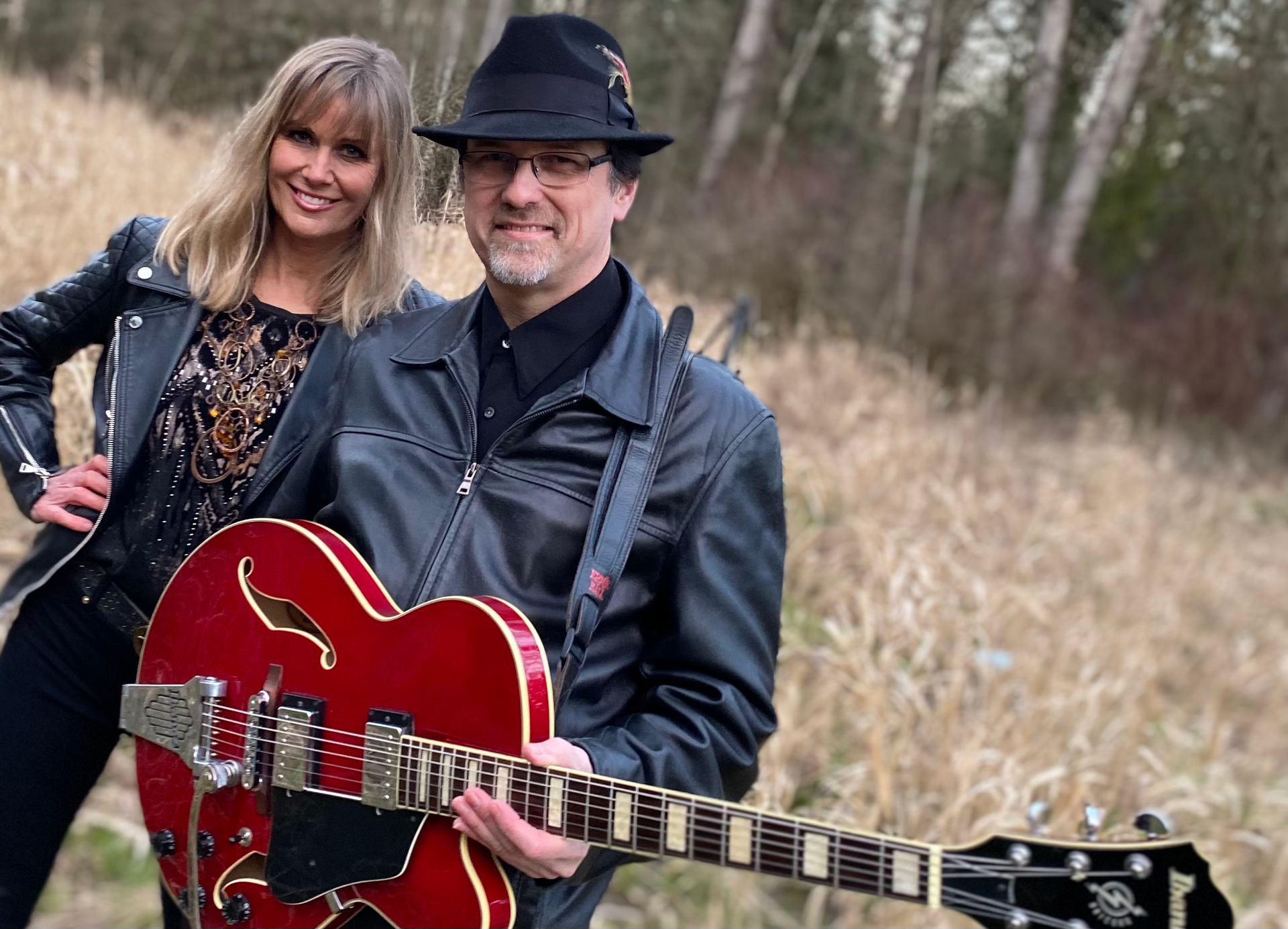 A man and a woman are standing next to each other in a field holding guitars.