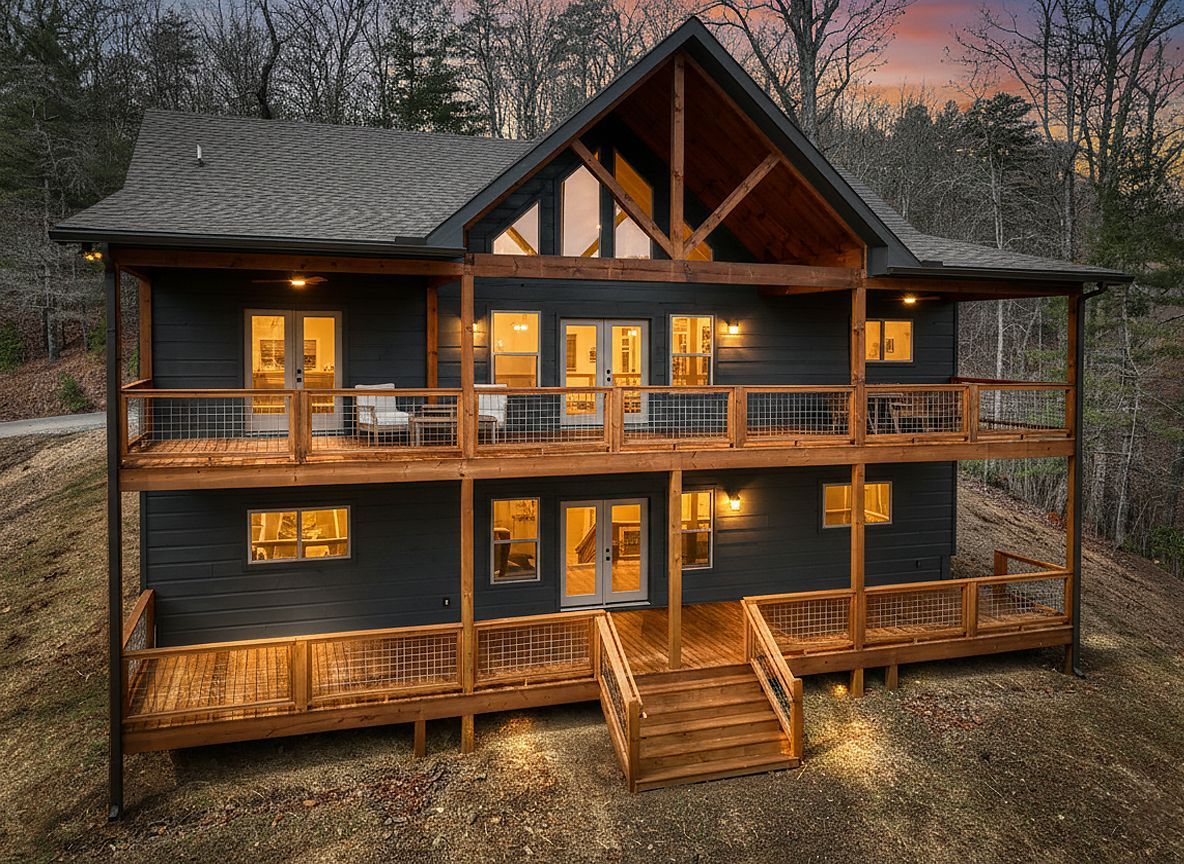 Wooden cabin with lit windows and wraparound porch at dusk, set among trees