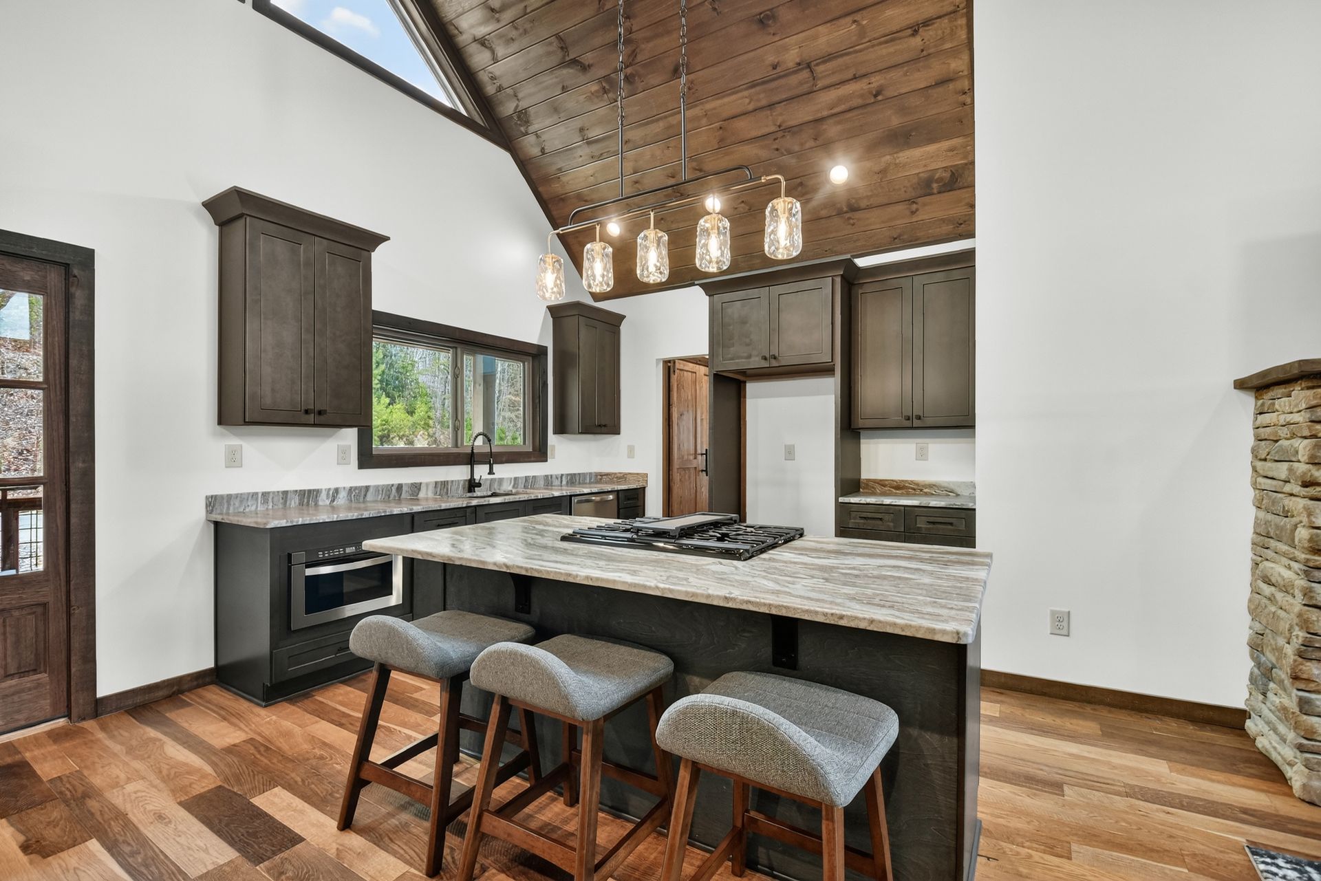 Modern kitchen with wood ceiling, granite island, pendant lights, and barstools