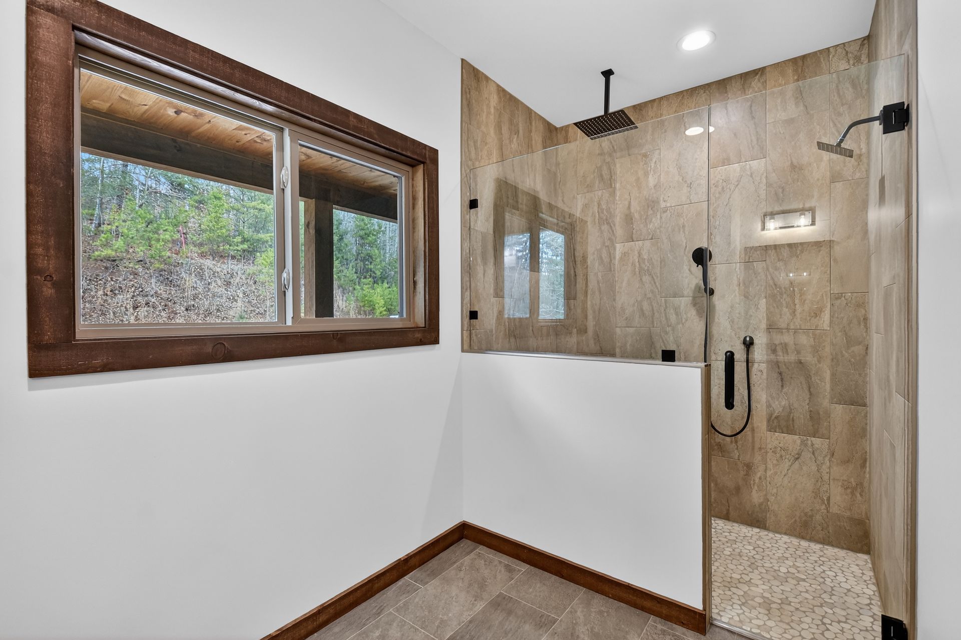 Modern bathroom with glass shower, beige tile, and wood-trimmed window.