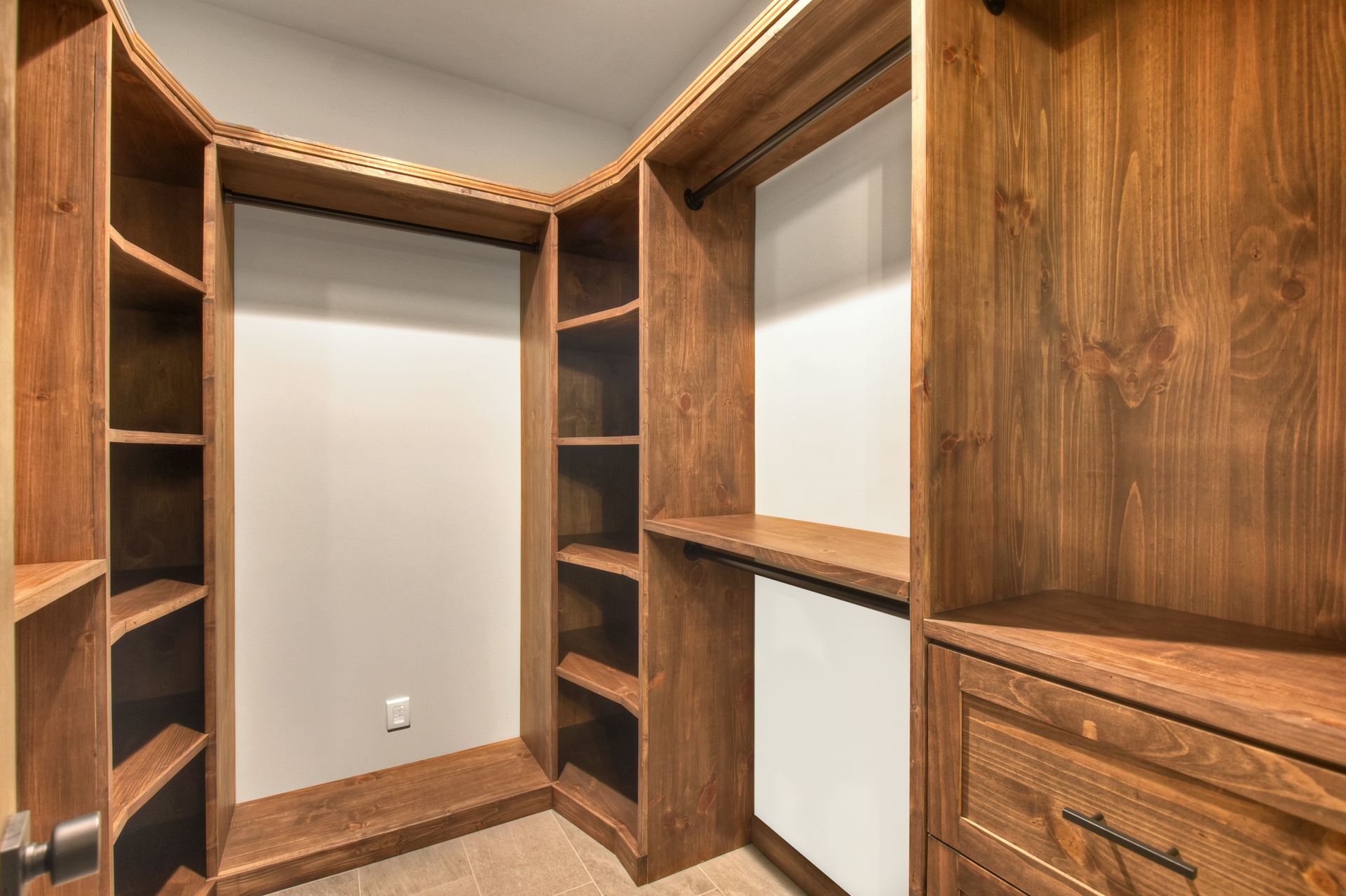 Built-in wood closet with shelves, hanging rods, and drawers in a small empty room