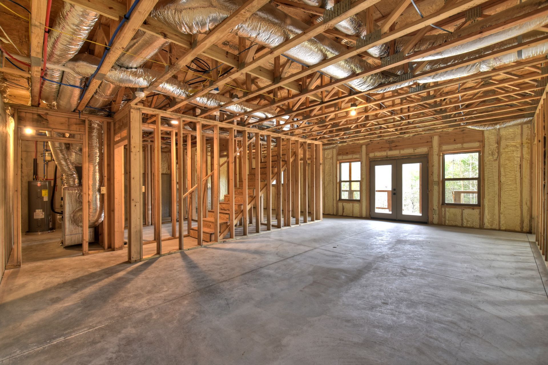 Unfinished house interior with exposed wooden framing, concrete floor, and daylight from windows and glass doors