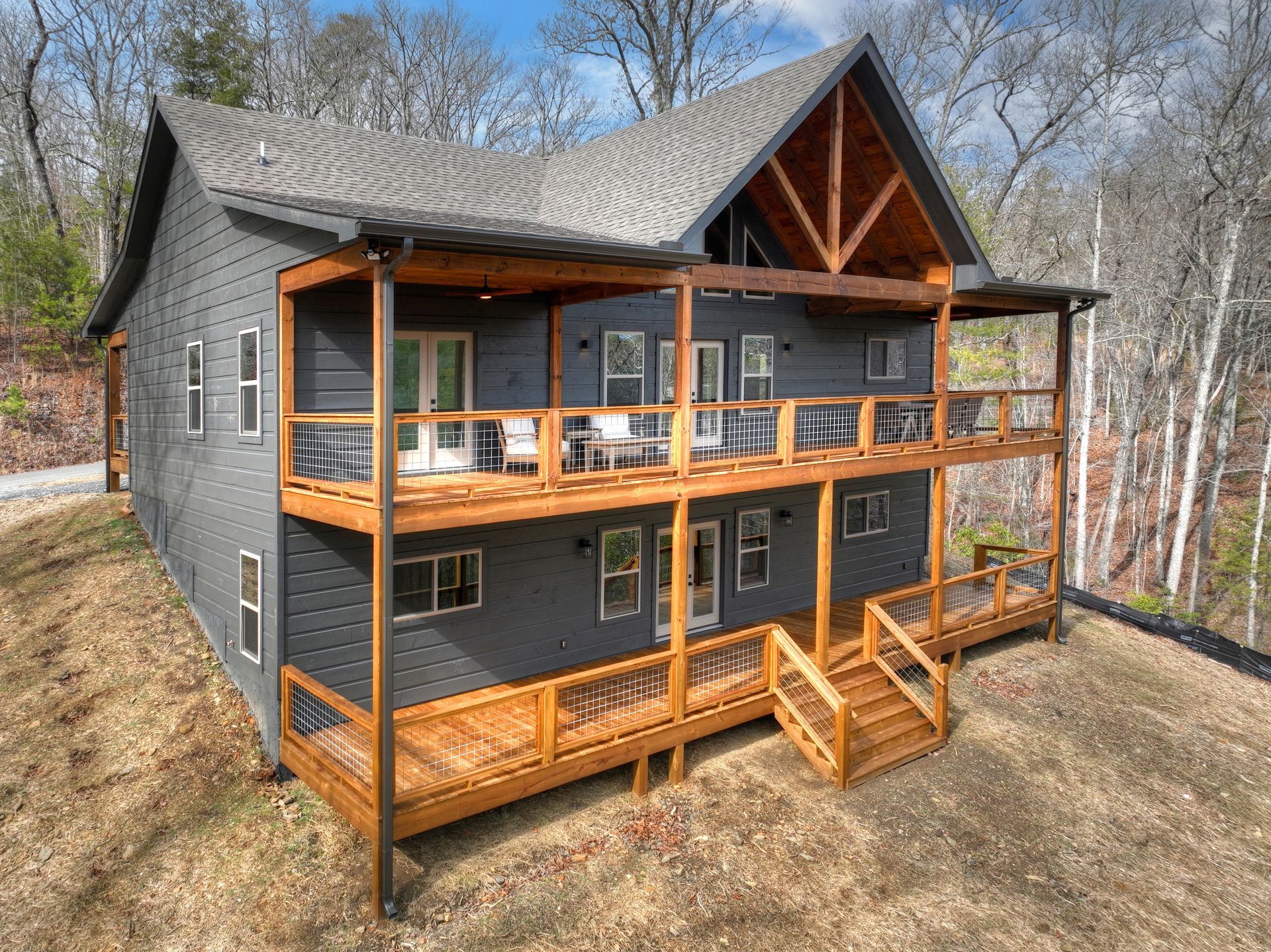 Modern dark gray cabin with wood decks and balconies in a wooded hillside setting