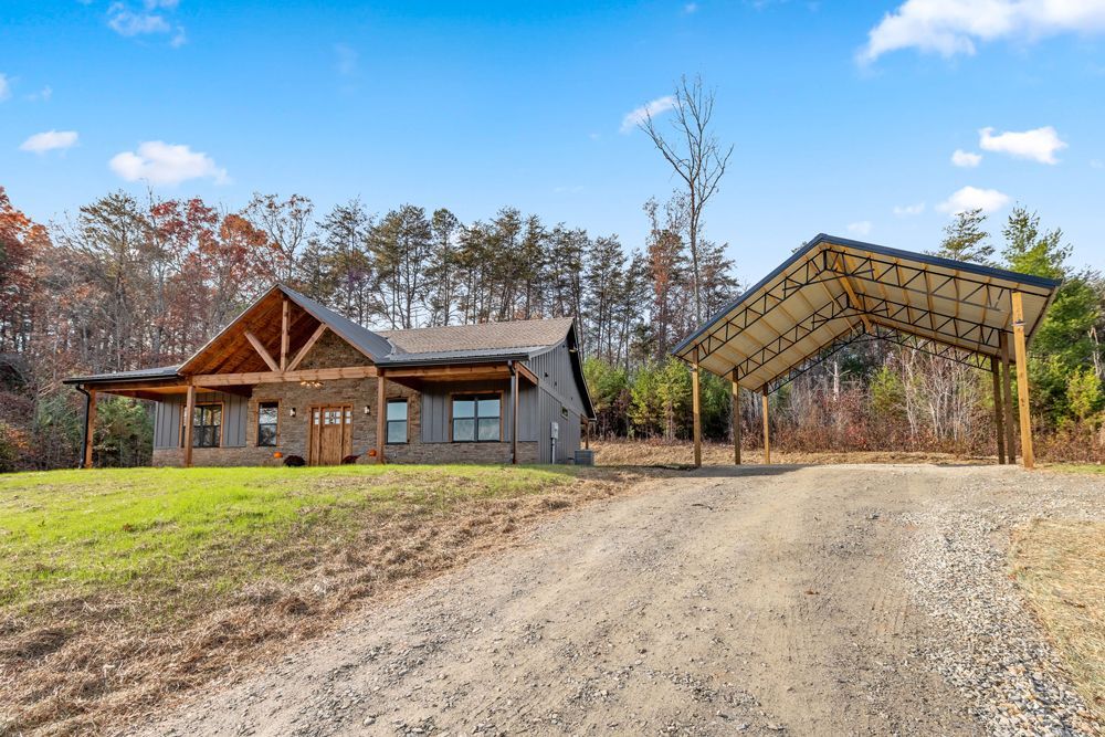 Rustic cabin and open pavilion on a gravel driveway with autumn trees in the background