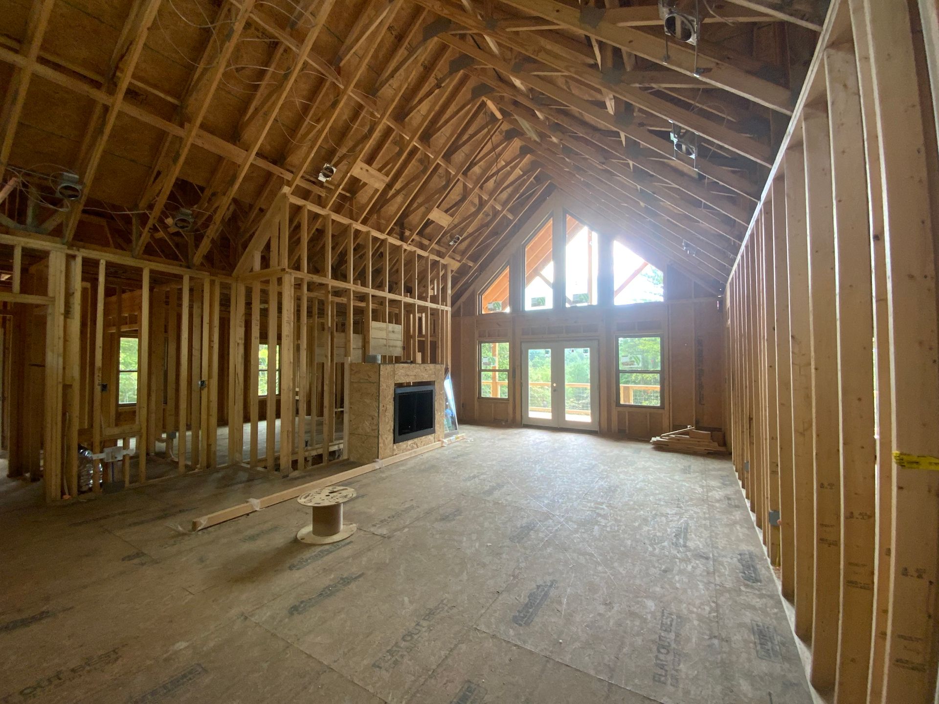 Unfinished attic interior with exposed wooden framing, sloped ceiling, and large windows at the far end.