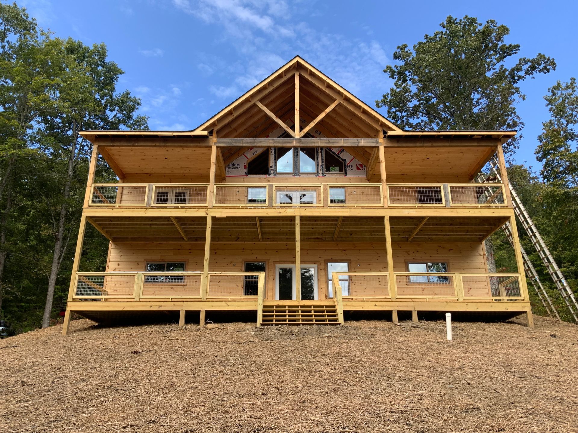 Large wooden cabin under construction on a hillside, with a covered porch and blue sky above.