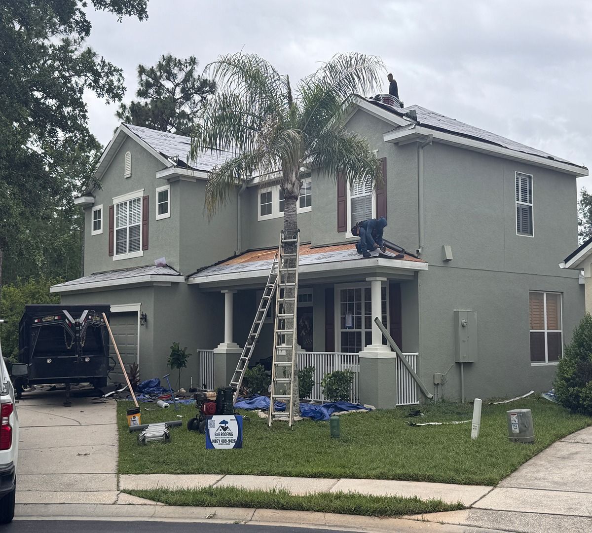 Two-story house with workers on the roof, ladders, and a black SUV in the driveway