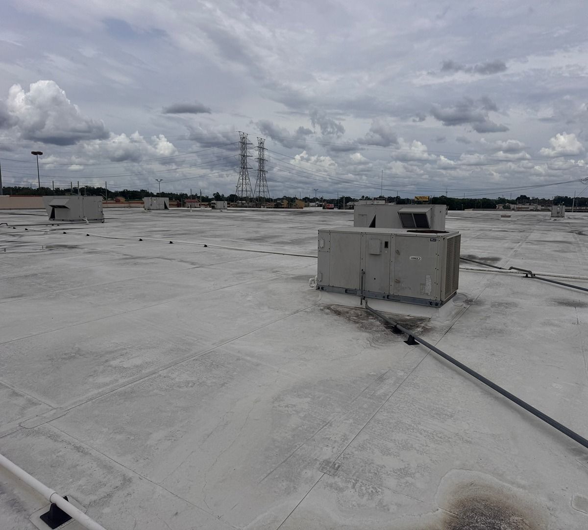 Flat white rooftop with HVAC units and power lines under a cloudy sky
