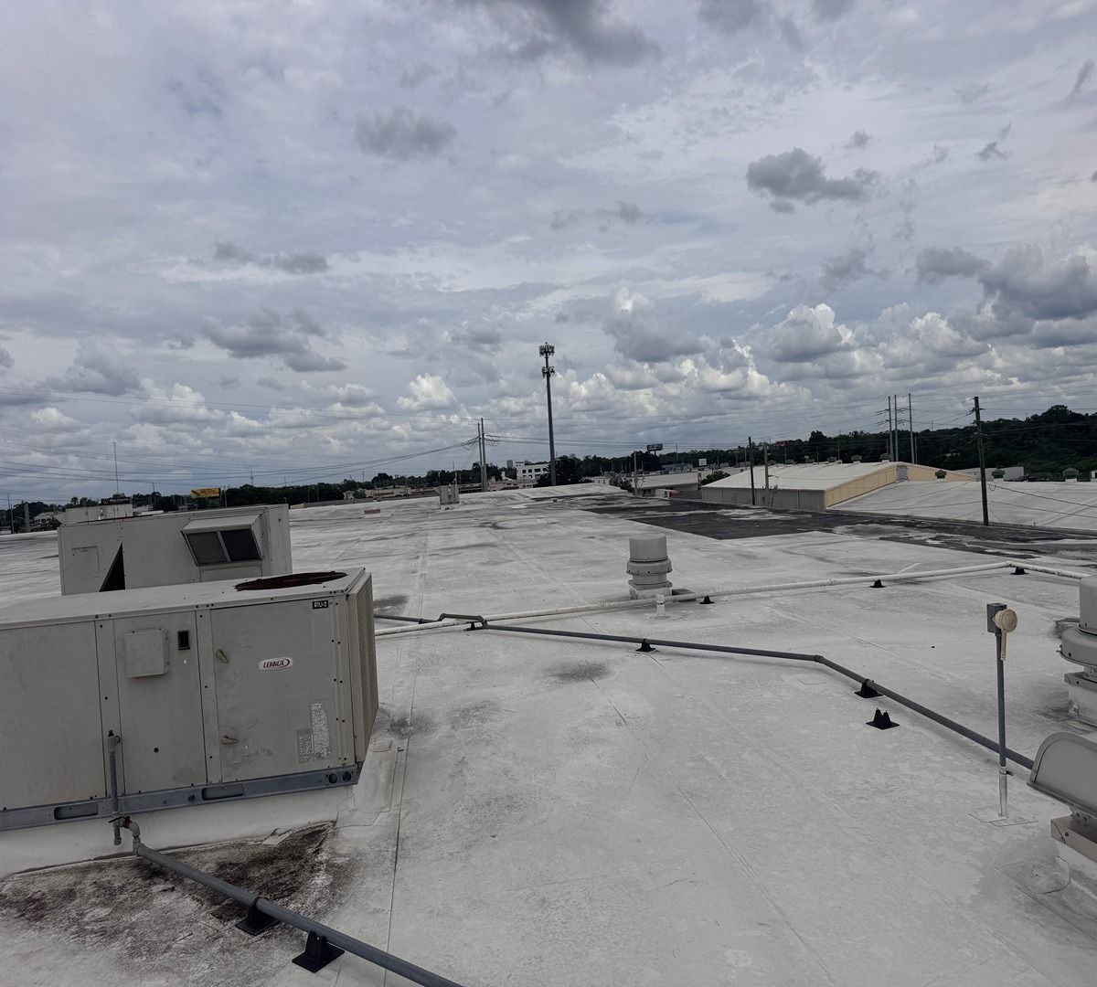 Cloudy rooftop with white roofing, HVAC units, and distant skyline under overcast sky