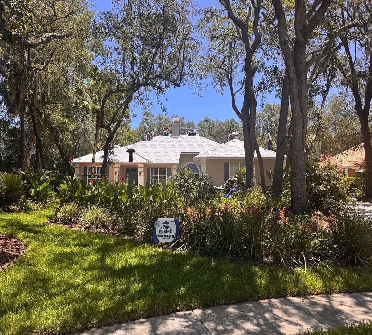 Single-story white house behind lush trees and garden in bright daylight