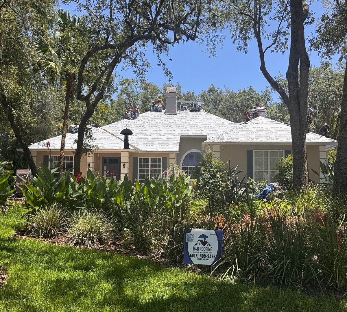 White cottage with a garden and trees under a blue sky, with a small sign in front