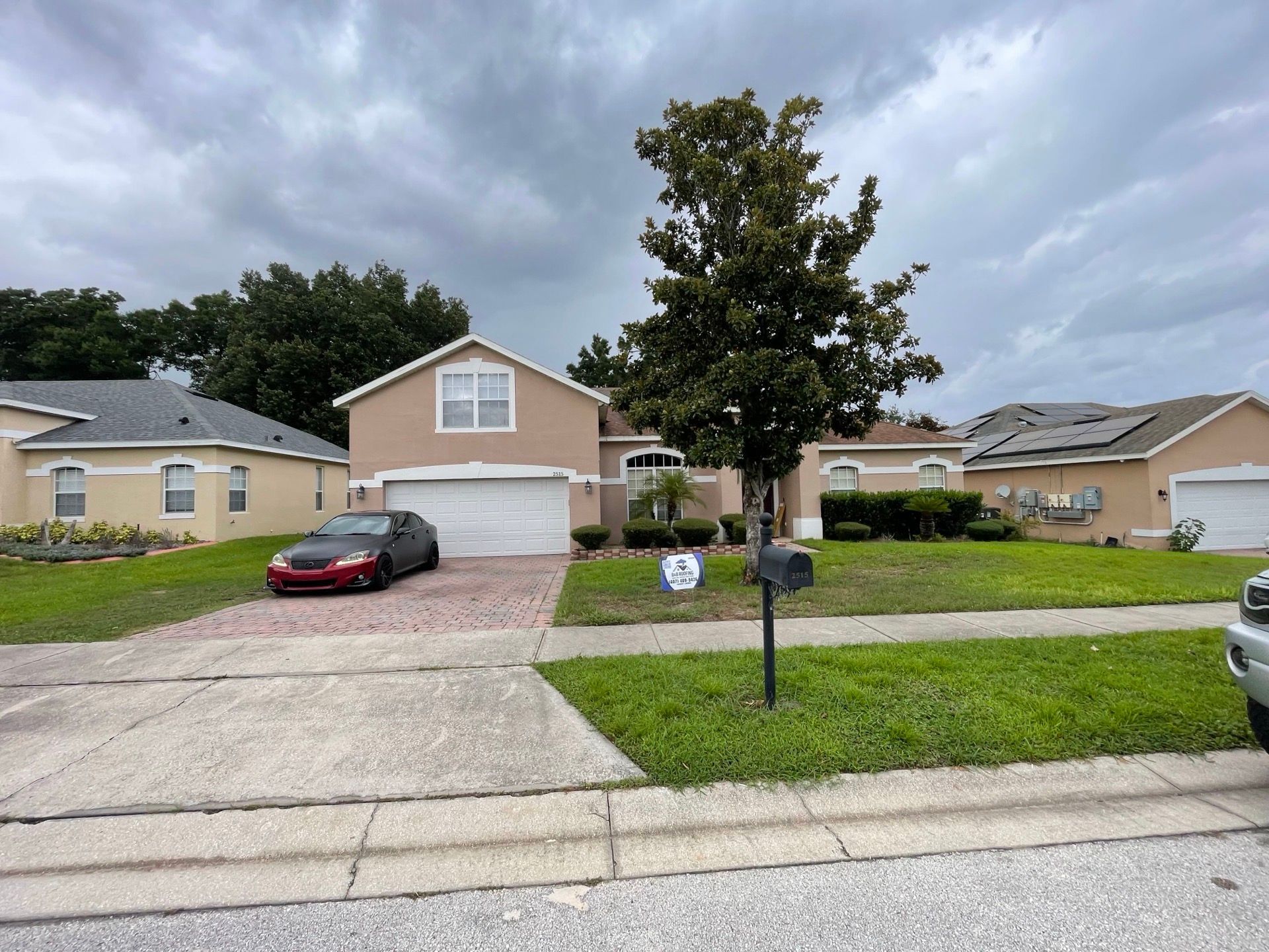 Suburban house with two cars in the driveway and a tree in the front yard.