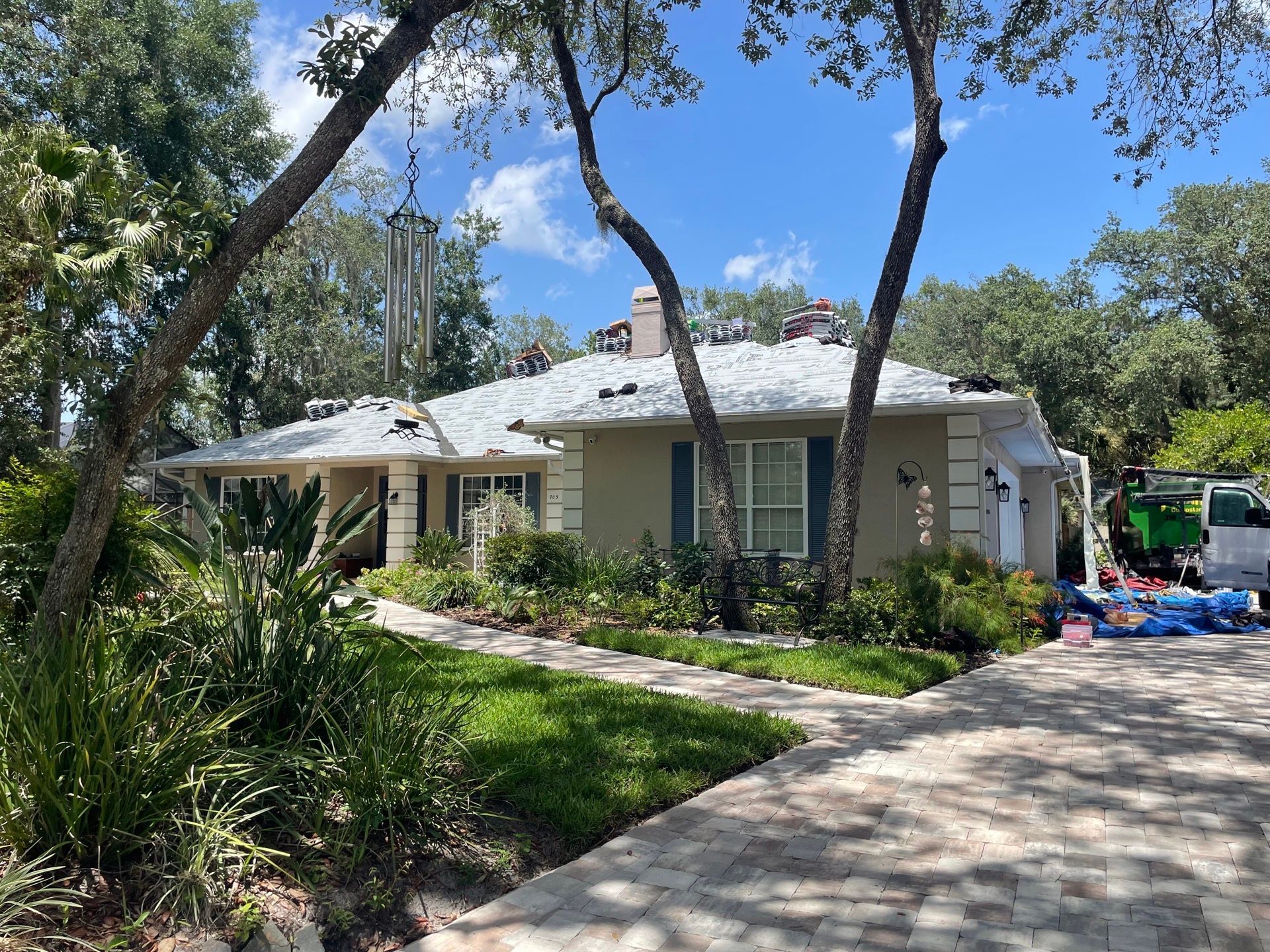 Single-story white house with a curved driveway, palm trees, and a sunny yard under blue sky