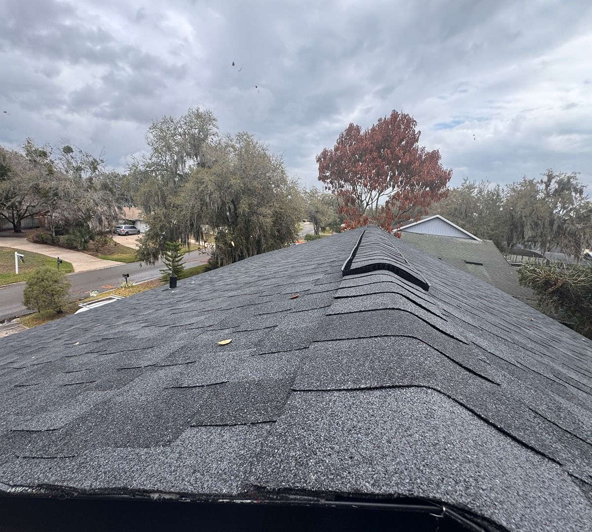 View from a shingled roof over a cloudy suburban neighborhood with trees and houses