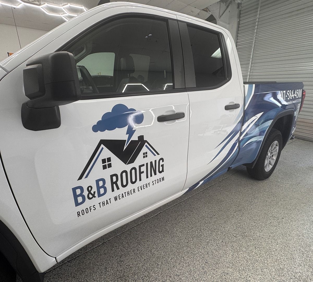 White B&B Roofing pickup truck with blue roof logo and company name on the door inside a garage