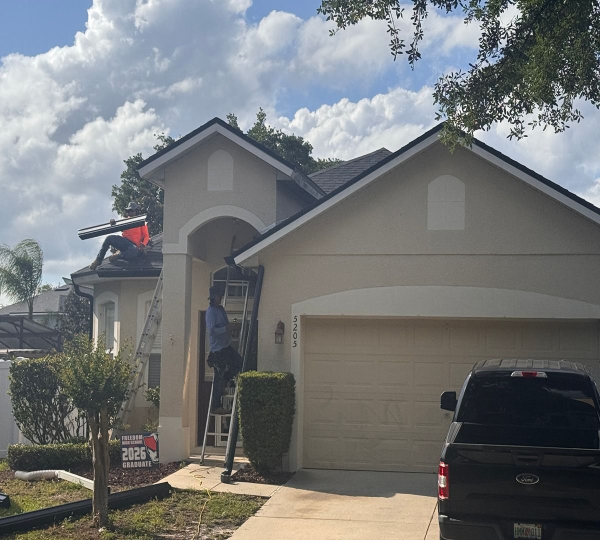 Suburban house with beige garage, a worker on a ladder, and a black SUV in the driveway