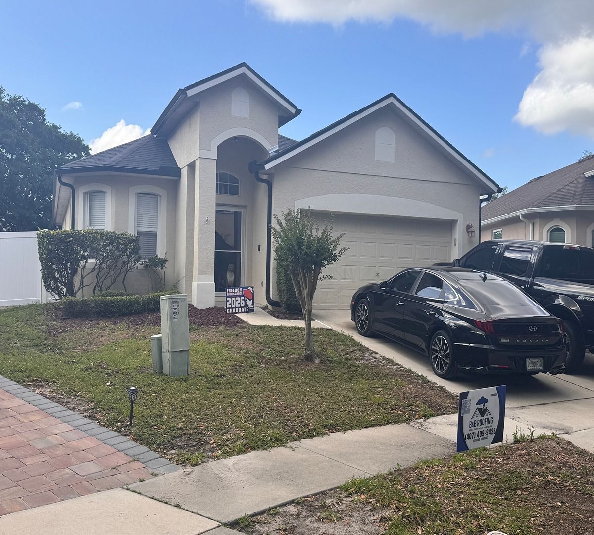 Suburban house with white garage, black car in driveway, and small front yard under a cloudy sky