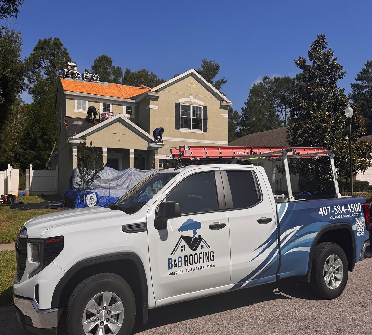 Blue-and-white roofing service pickup truck parked in front of a house with a roof under repair