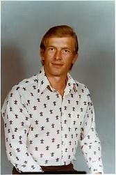 Portrait of a man in a white patterned shirt against a gray studio background