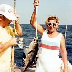 Two people on a boat hold up a large fish on a fishing line, with the ocean behind them.