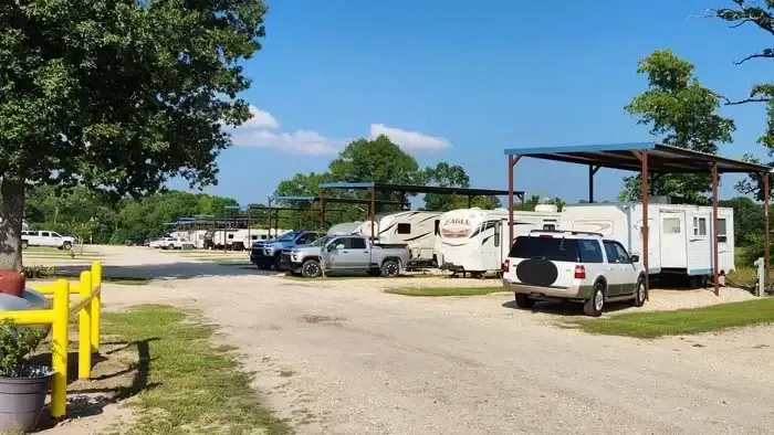 RVs and cars parked beside a gravel road under a metal canopy on a sunny day