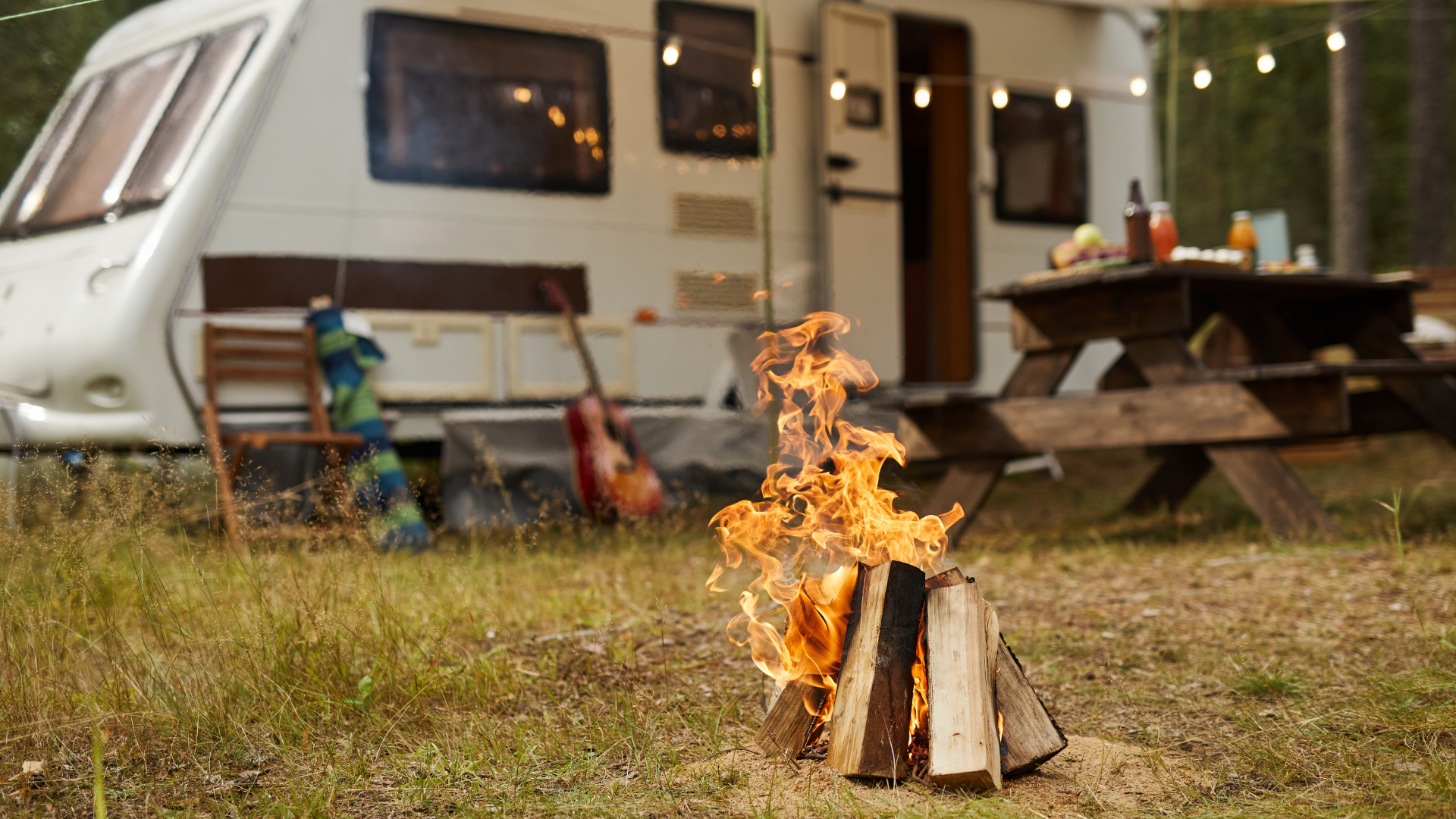Small campfire burning in front of a camper and picnic table at an outdoor campsite.