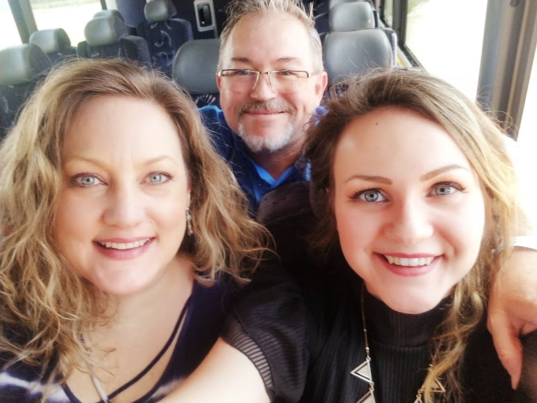 Three smiling people posing closely together in a car interior