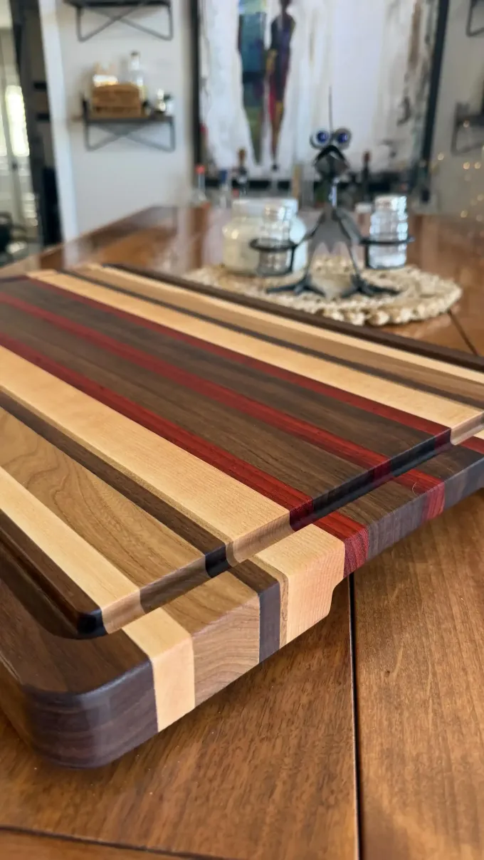 Wooden cutting board with multicolored stripes on a table, beside a mirror and candles in the background