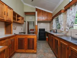 Wood-paneled kitchen with wooden cabinets, tiled floor, and a black stove beneath a window