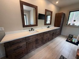 Wooden double-sink bathroom vanity with white countertop, black faucets, and wall mirrors.