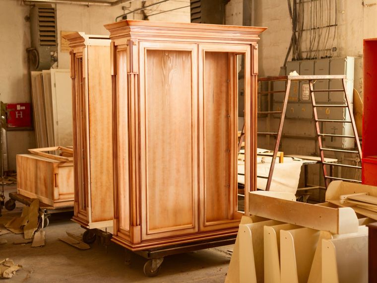 Wooden cabinet in a workshop with ladders and cardboard boxes nearby