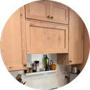 Wooden kitchen cabinets above a countertop with a small shelf of bottles and jars, framed in a circular crop