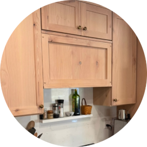 Wooden kitchen cabinets above a countertop with a small shelf of bottles and jars, framed in a circular crop