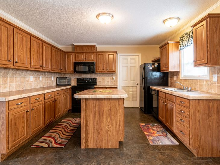 Spacious kitchen with oak cabinets, black appliances, and a central island under warm ceiling lights