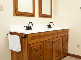 Wooden double-sink bathroom vanity with white countertop, black faucets, and wall mirrors.