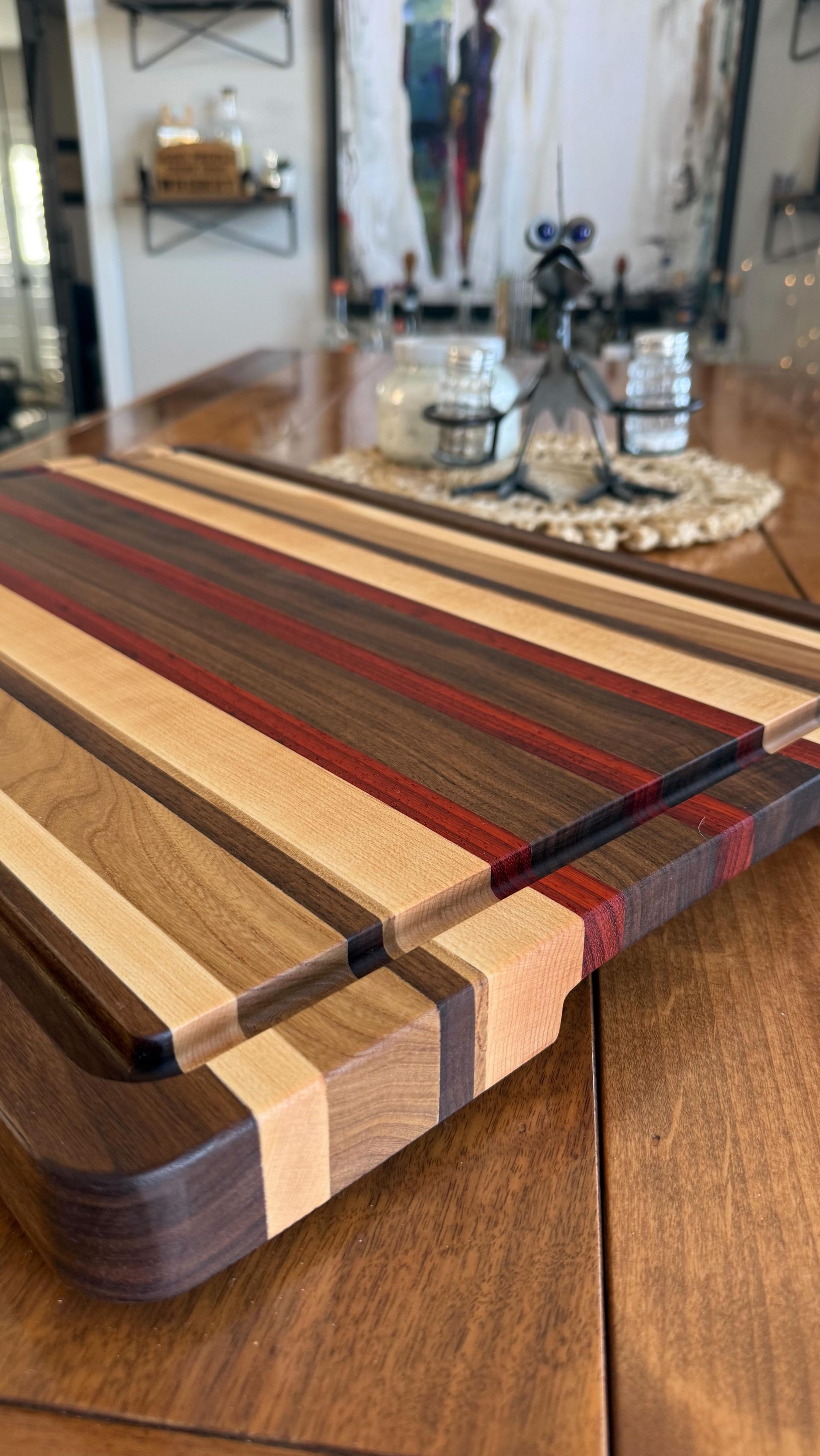 Wooden cutting board with multicolored stripes on a table, beside a mirror and candles in the background