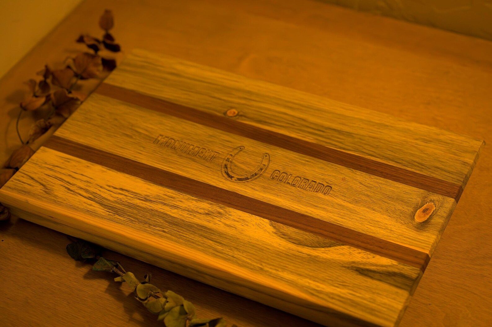 Wooden cutting board with a metal handle, lit by warm orange light on a table