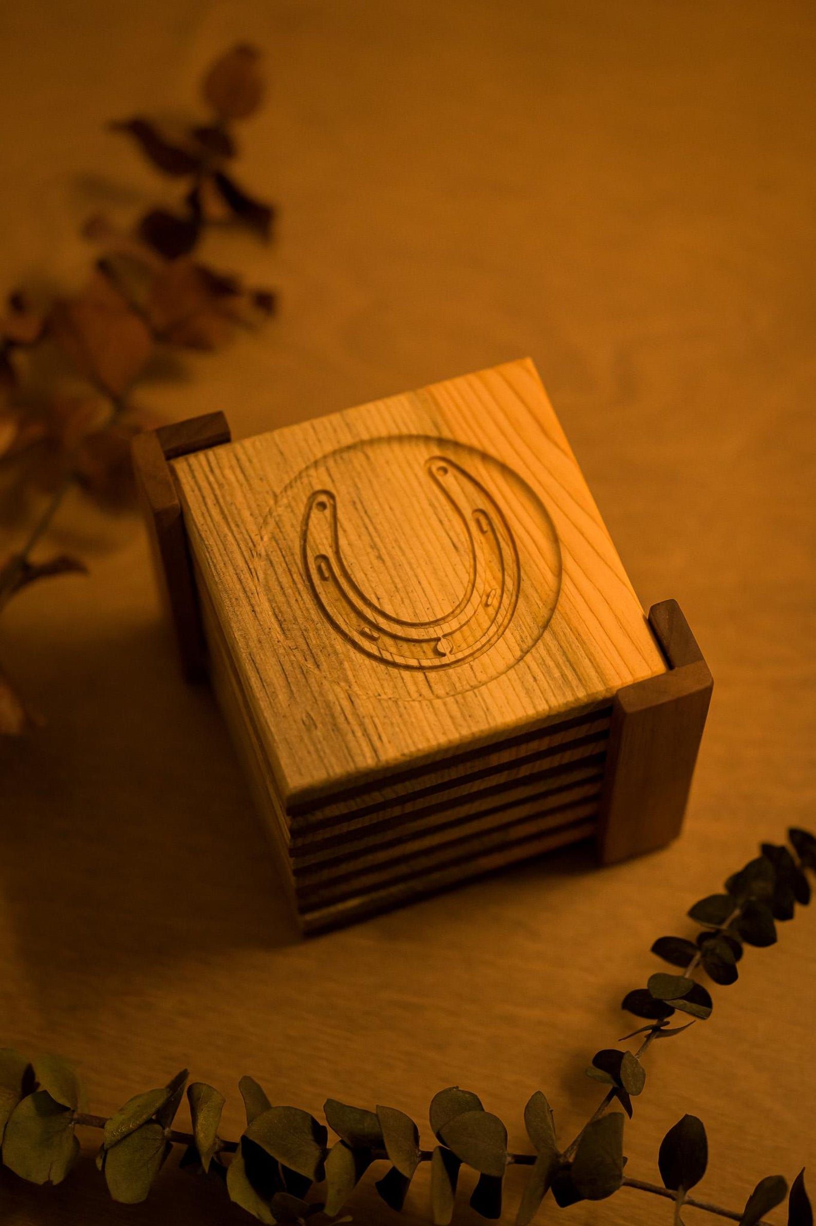Wooden coaster with engraved crescent moon on a warm, amber-lit table, framed by dried leaves.