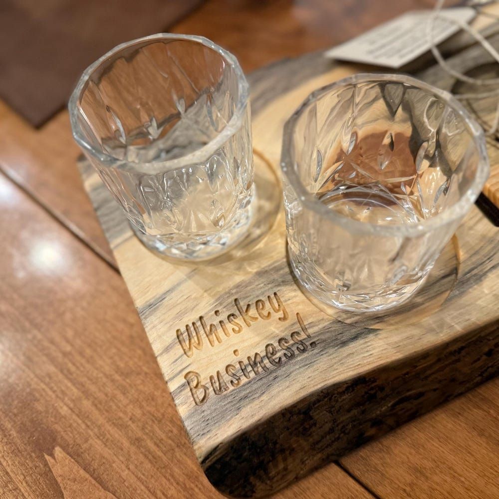 Two whiskey glasses on a wooden board engraved “Whiskey Business”