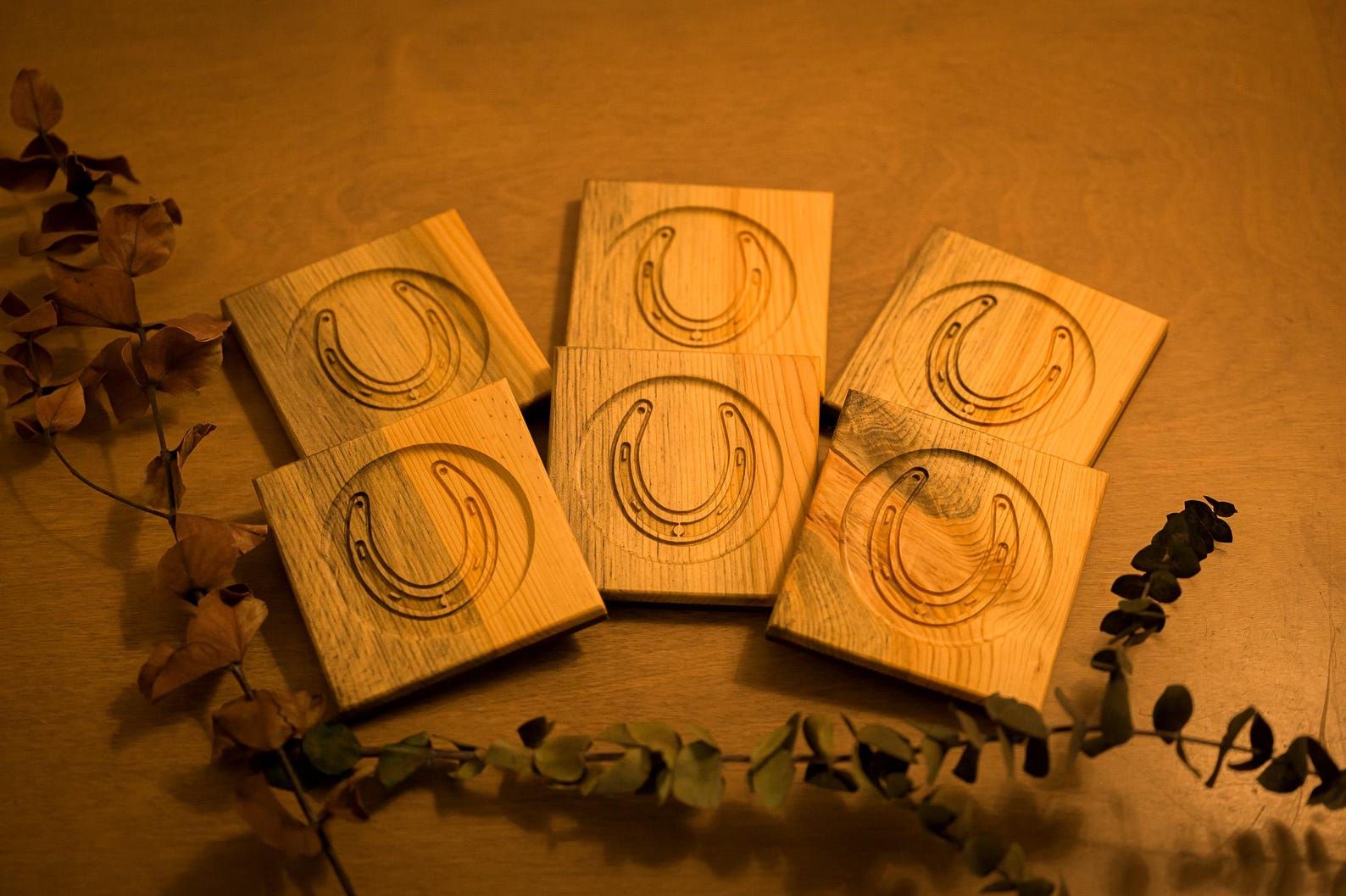 Five small paper packets on a warm brown surface, decorated with circular sketches and surrounded by dried leaves.
