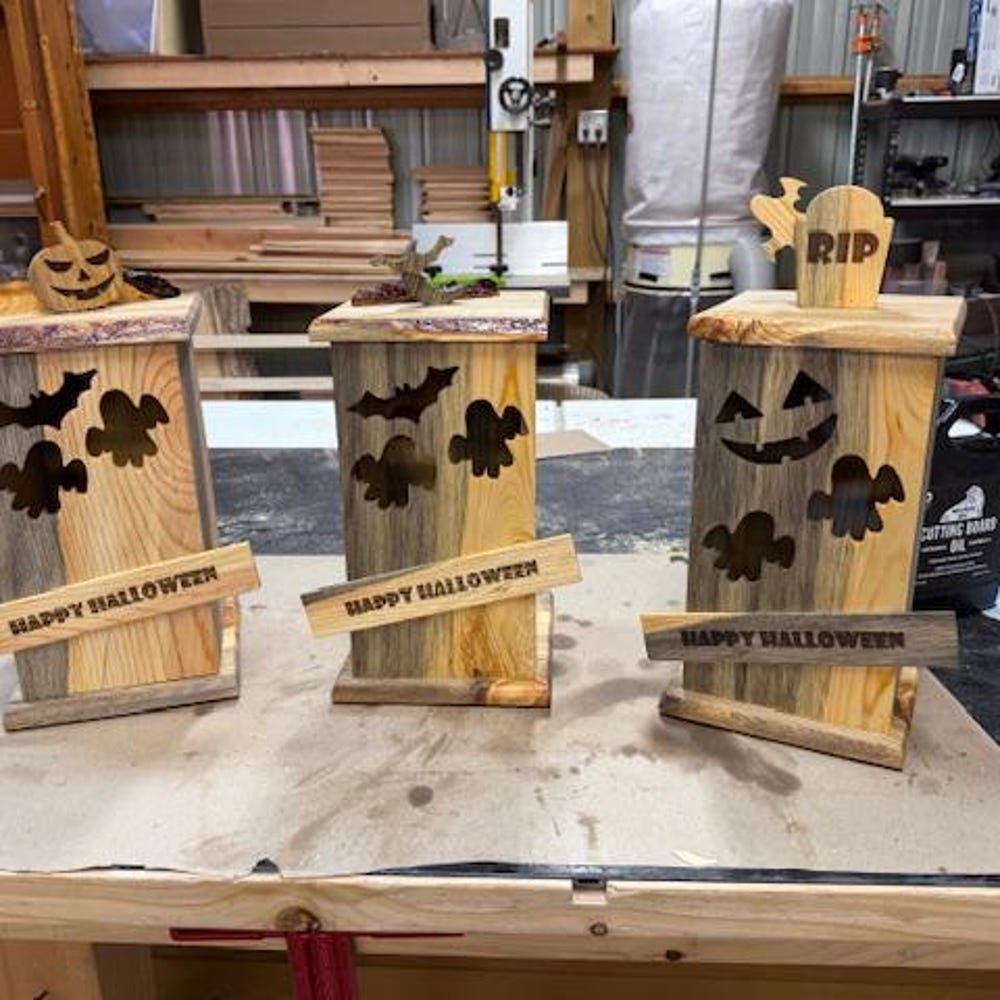 Three small wooden Halloween lanterns with jack-o’-lantern cutouts and “Happy Halloween” signs on a workbench