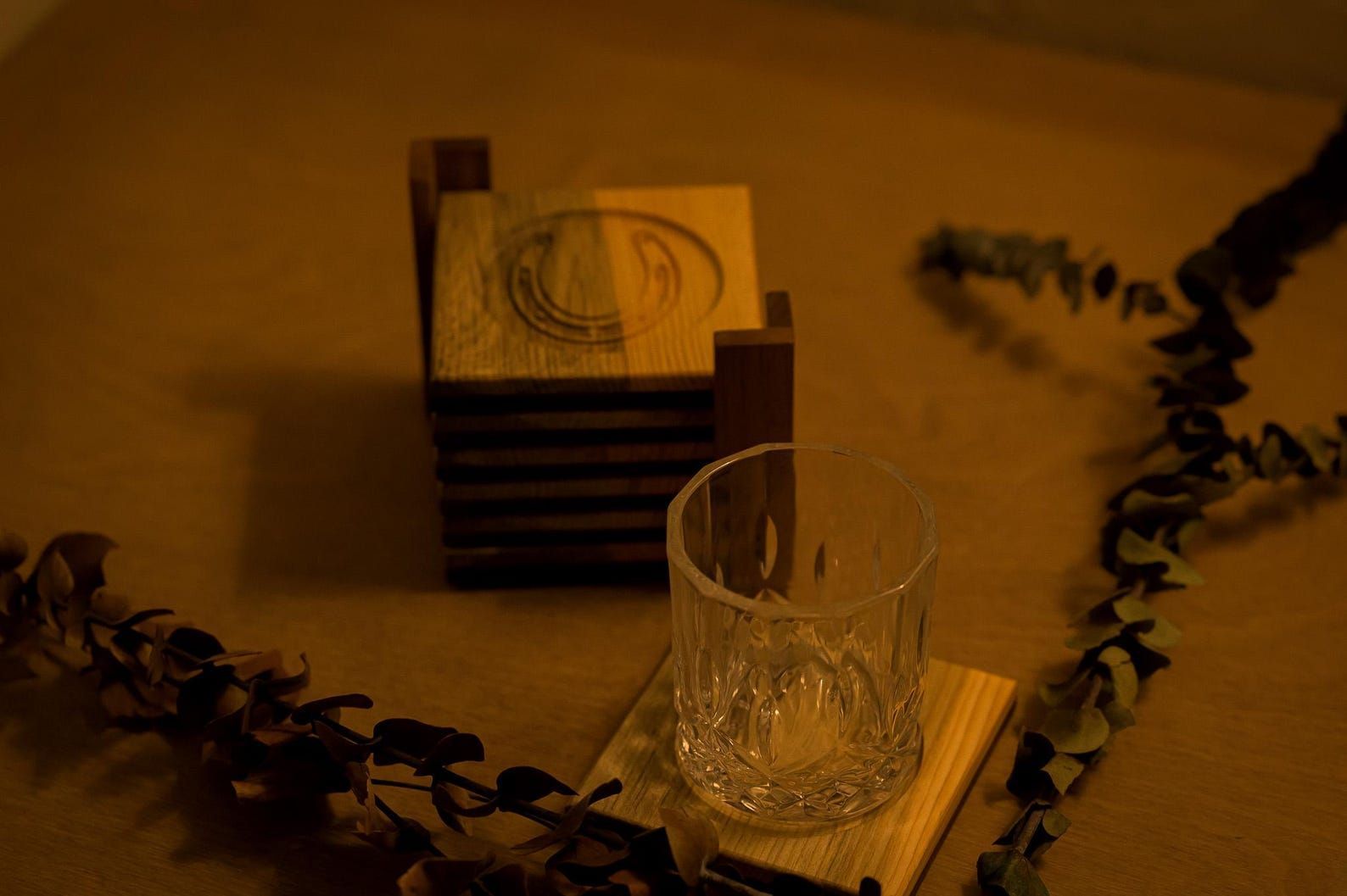 Glass and stacked boxes on a warmly lit table with dark foliage around them
