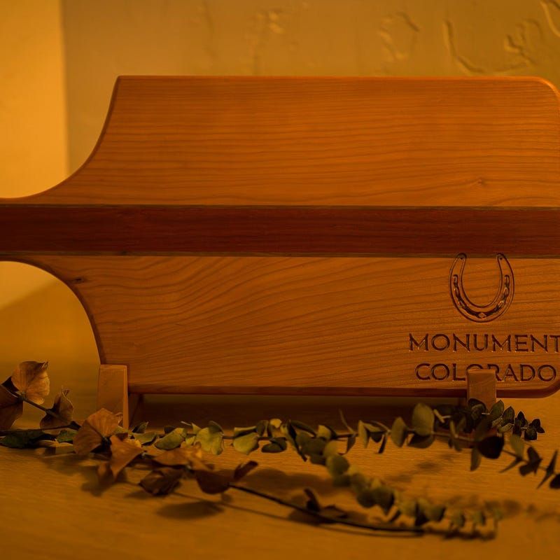 Wooden sign with “Monument Colorado” under warm orange lighting, with leaves in the foreground