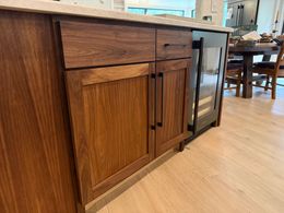 Wood-paneled kitchen with wooden cabinets, tiled floor, and a black stove beneath a window