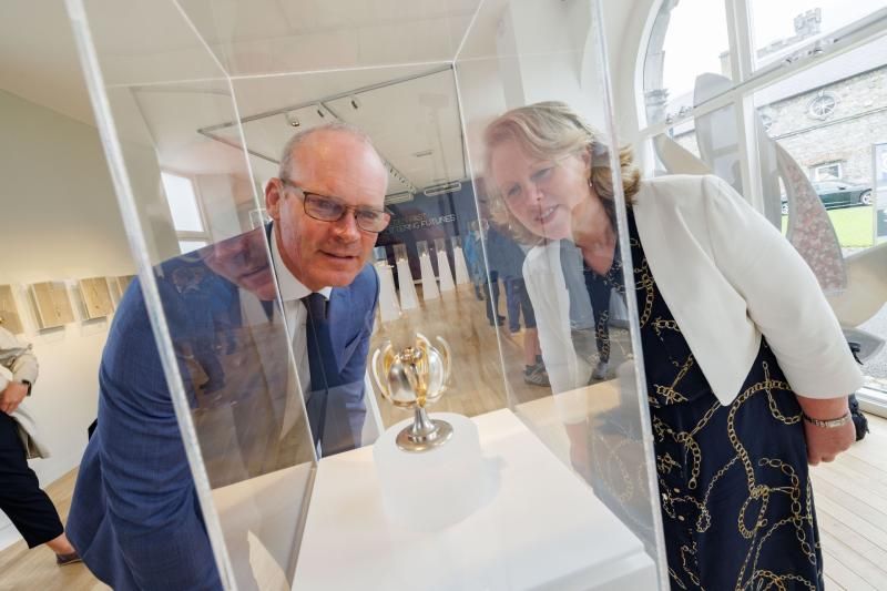 Two people lean toward a small trophy displayed under glass in a bright room.