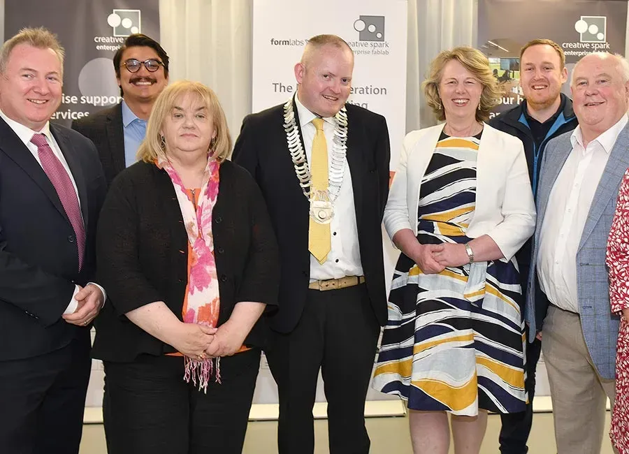 Six people standing in a row at an event, dressed in formal attire, in front of a branded backdrop
